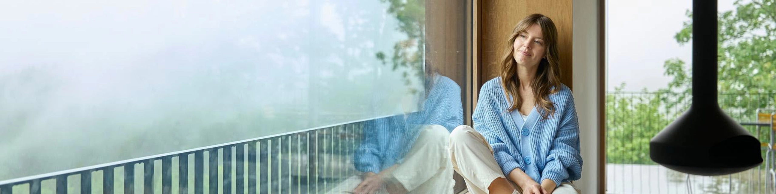 Symbolbild für finanzielle Entlastung: Frau sitzt ruhig am Fenster nach erfolgreicher Kreditanfrage