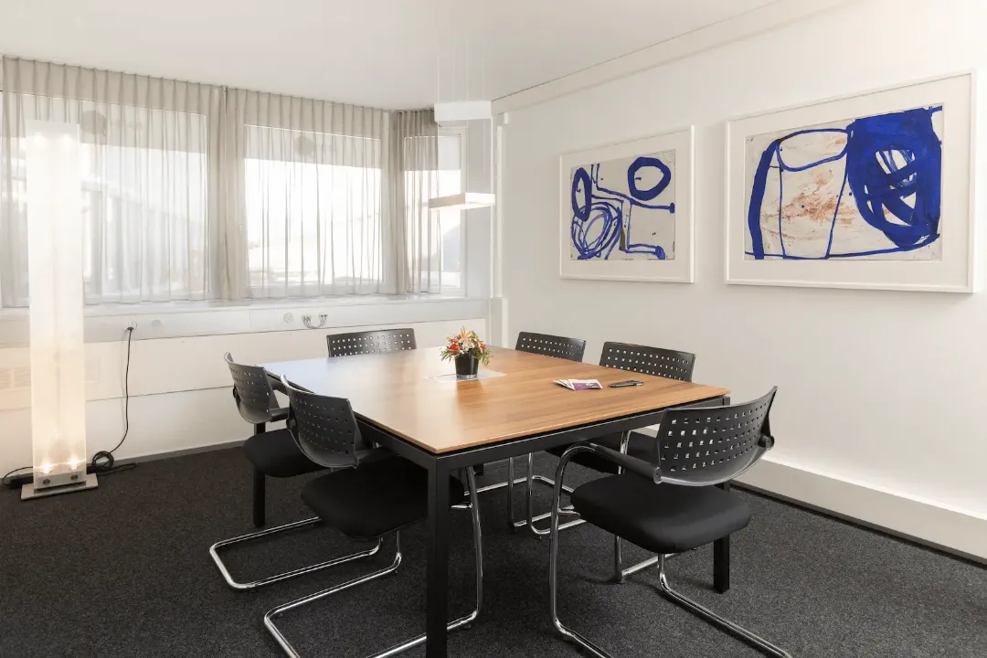 Besprechungsraum der BANK-now Filiale Chur mit grossem Tisch, mehreren Stühlen und Wandbildern.