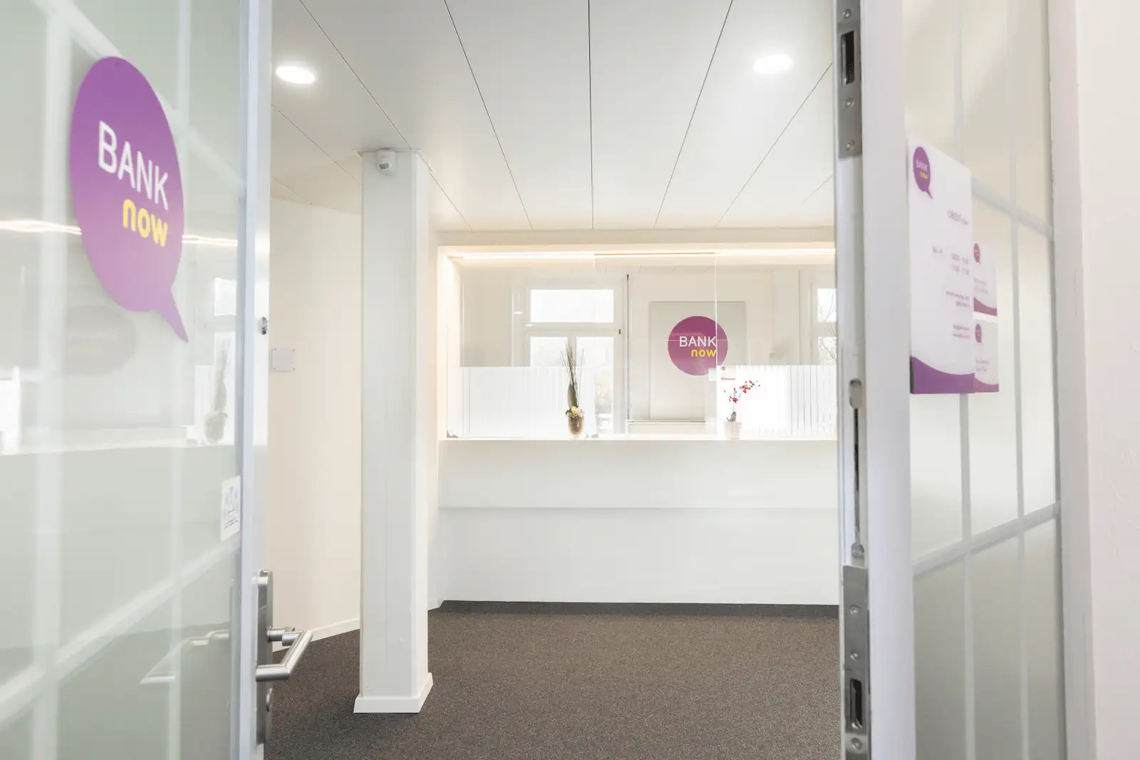 Heller Schalterbereich der BANK-now Filiale Luzern mit Empfangstheke und Glaswand.